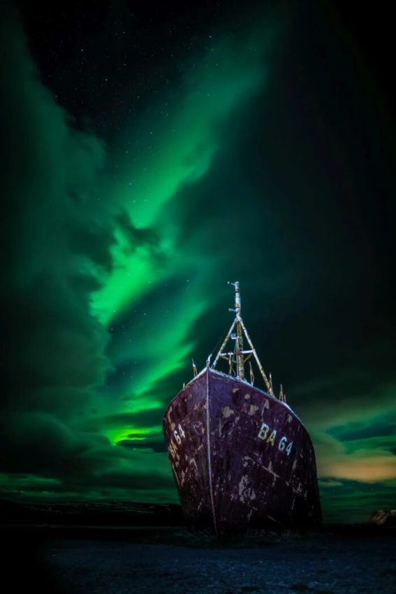 Una saga islandesa (Carl Gallagher): Imaxe que mostra a aurora boreal brillando a través dun oco nas minchas sobre os restos do naufraxio do outrora baleeiro Gardur na costa de Islandia.