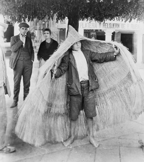 Neno suxeitando unha capa para a choiva feita de palla. Imaxe: Ruth Matilda Anderson, a través da Hispanic Society of America